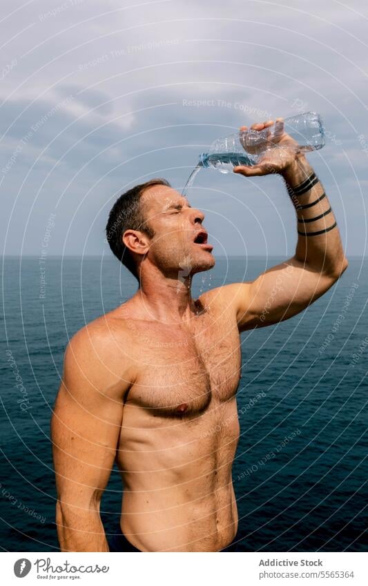 Man refreshing with water with ocean background. man sky cloudy splash face standing fitness hydrate thirsty wellness summer heat relief moment break exercise