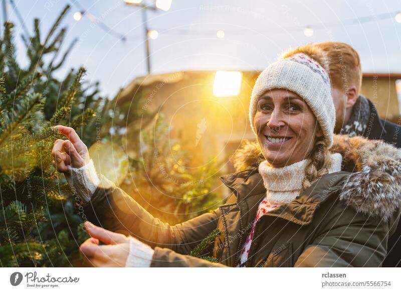 Happy woman and her Boyfriend want to buy a Christmas tree and look into the camera redhead tradition choice smile love couple purchase farm pine tree norway