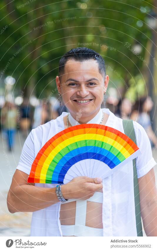 Happy adult man with a LGBT pride fan Man cheerful crowd urban white shirt earring smile joy celebration LGBTQ vibrant color outdoors event happiness expression