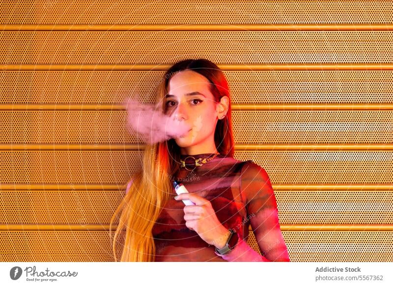Young woman vapor exhales against orange backdrop background textured vibrant hair style attire confident young fashion smoke e-cigarette modern urban pattern