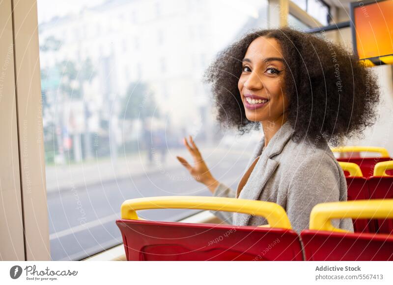 Happy afro woman while sitting on bus seat curly hair window reflection city transportation joy daydream red commute public travel urban journey coat grey