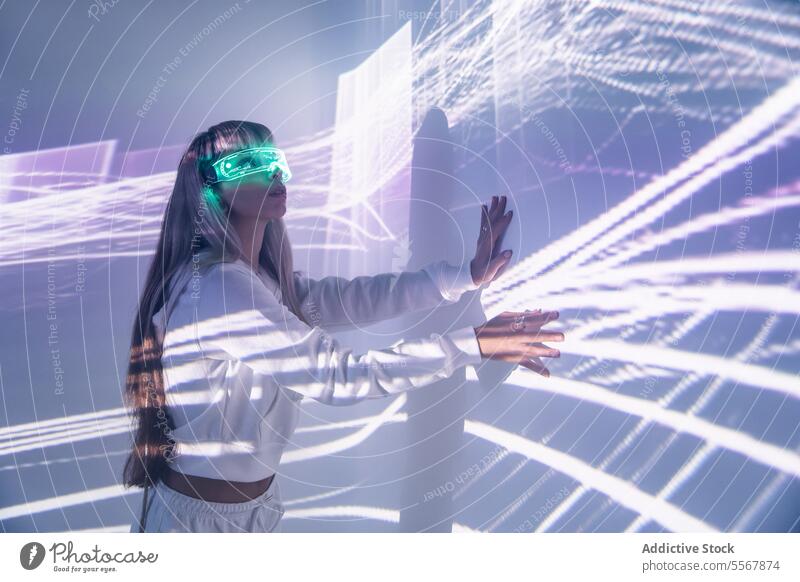 Woman in VR goggles touching wall with lights woman vr glasses futuristic explore cyberspace studio shot imagine long hair bangs trendy style blonde headset