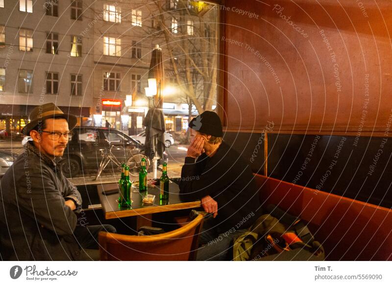 Two men sit at the window of a bar in Berlin and drink beer Autumn Prenzlauer Berg Bar Roadhouse Café chestnut avenue Evening Town Downtown Capital city