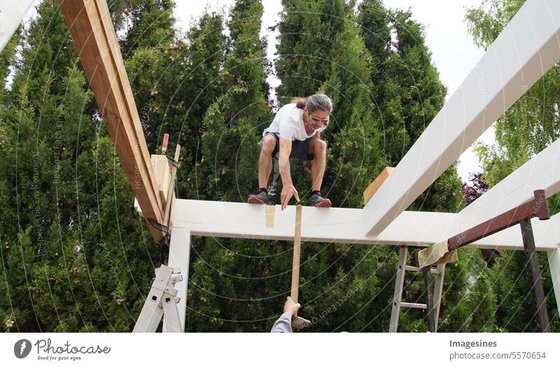 Balance. Male worker standing on wooden beam construction for carport. Handing over the hammer on the construction site. Occupational safety concept balance