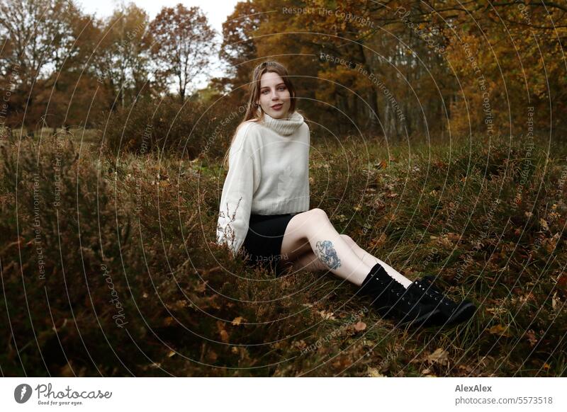 Young woman in white wool sweater and black skirt sits in the grass between heather in a northern German heath landscape in fall Woman Large tall woman
