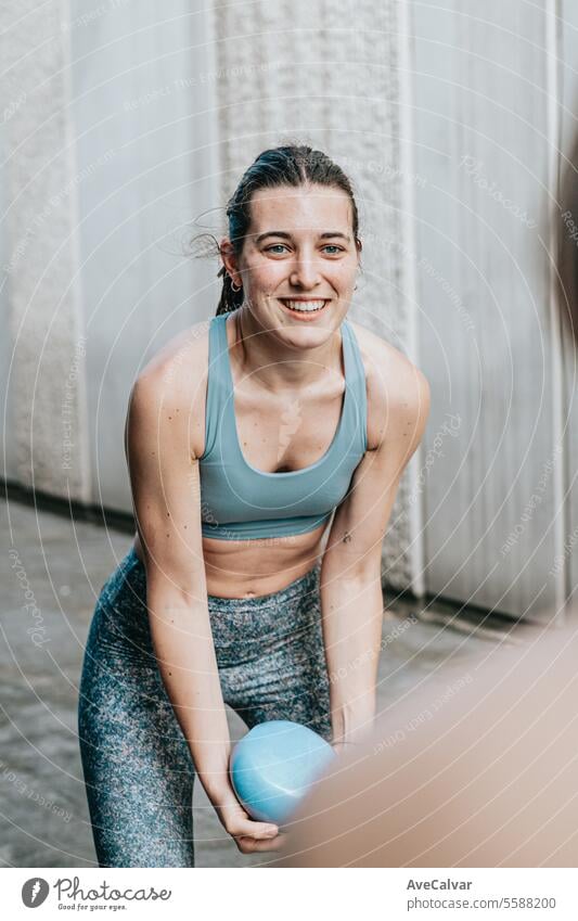 Smiling athletic girl doing series of exercises with a medicine ball on  training day. Urban scene. - a Royalty Free Stock Photo from Photocase