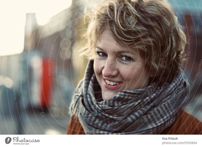 "WELL, WHAT DO YOU WANT AGAIN?" Woman Short-haired Grinning Brash Blonde Curl Cold Scarf Winter Smiling beautiful colours Happiness Colour photo Exterior shot