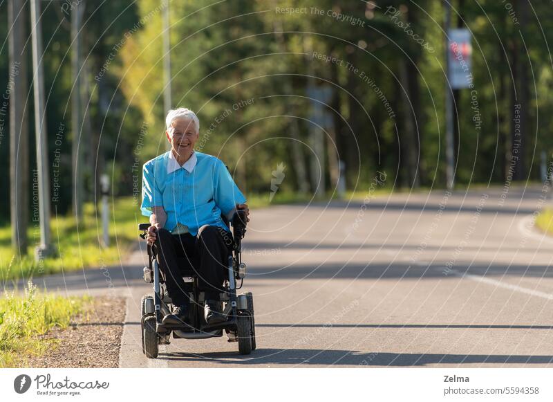 Smiling disabled old woman in a wheelchair on the highway senior invalid person asphalt road driving freedom elderly older happy active seniors female people