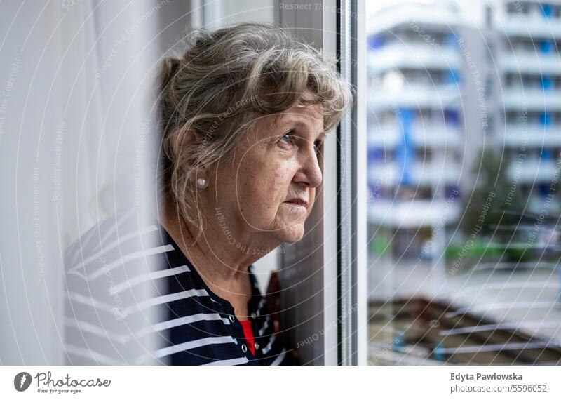 Portrait of senior woman looking through window real people mature female Caucasian elderly home house old aging domestic life grandmother pensioner grandparent