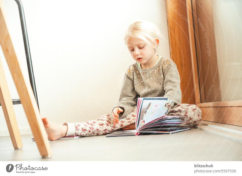 little girl sits on the floor and looks at a children's book Girl at home Joie de vivre (Vitality) Playing Contentment stay at home Parenting Happiness Child