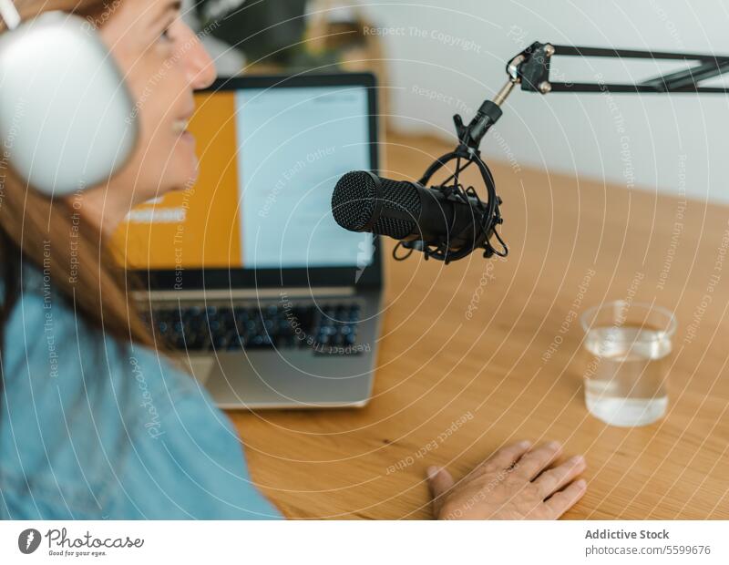 Woman recording podcast at table with mic woman microphone talk modern radio host speak female laptop broadcast work studio headphones device communicate