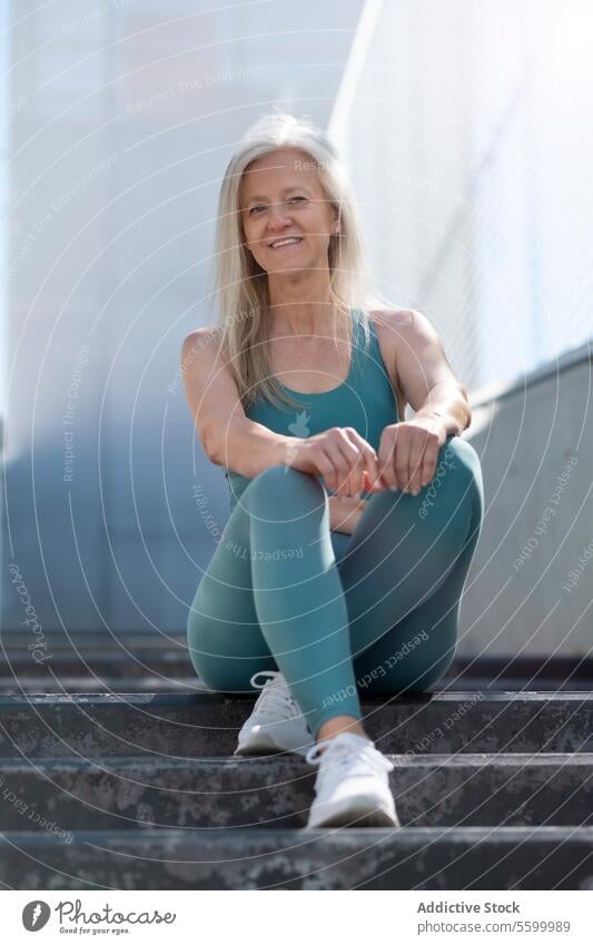 Active senior woman resting on steps after workout active fitness health wellness smiling sitting gray hair sportswear leggings tank top sneakers exercise