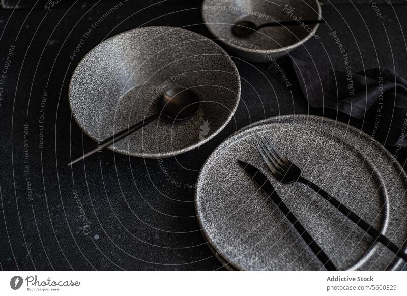 Modern dark tableware setup on a black background stoneware dishes utensils backdrop elegant cutlery arrangement sleek dining setting sophisticated plate bowl