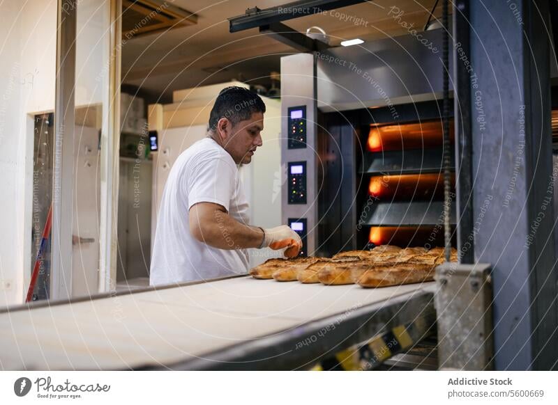 Latino baker taking bread out of the oven man latino conveyor belt equipment bakery picking automation industrial tray food technology business product factory