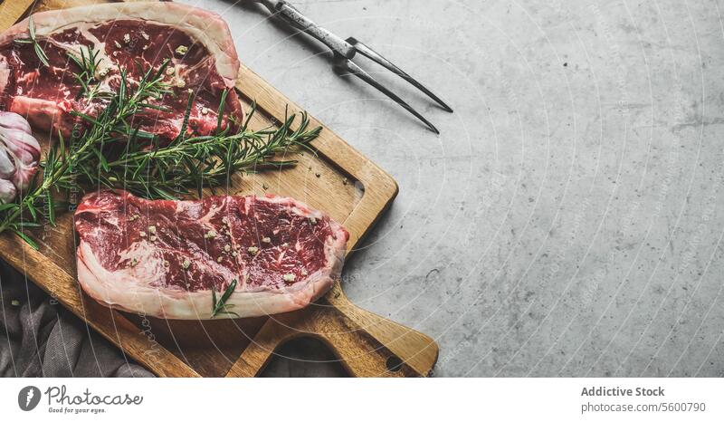 Raw beef steaks background with rosemary and green pepper on wooden cutting board with butcher fork. Close up. Preparing fresh meat. Top view with copy space.