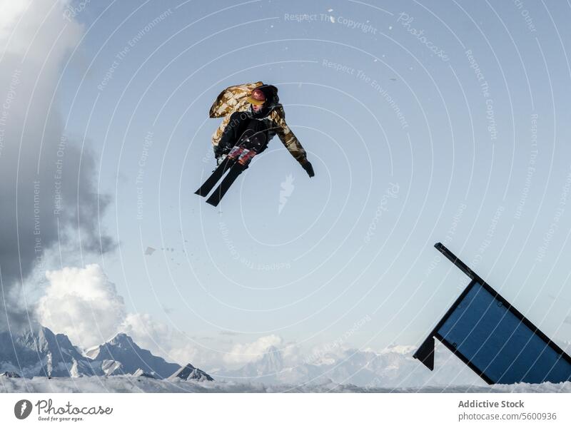 Anonymous man jumping with snowboard on Swiss Alps against blue cloudy sky anonymous snowboarder mountain blue sky sunlight vacation warm clothes peak full body