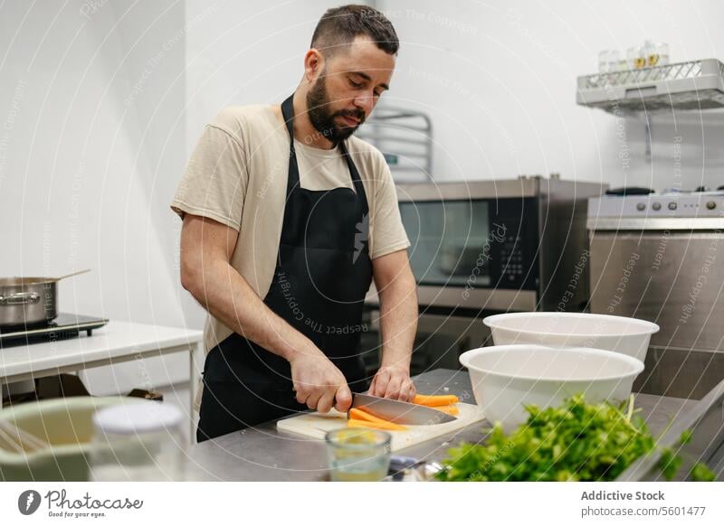 Young chef cutting carrots cook cooking kitchen food professional restaurant vegetables knife man young work male dish cuisine person job preparation meal