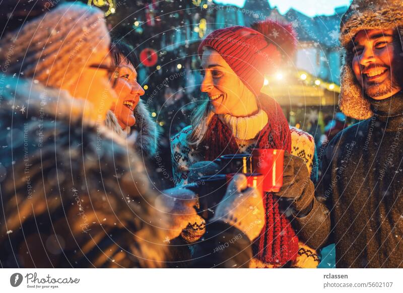 Cheerful friends enjoying mulled wine and hot chocolate in a snowy Christmas market punch merry christmas cup gloves traditional christmas market advent german