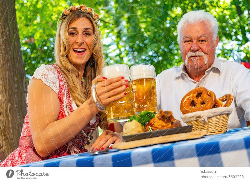 Bavarian women and old man clinking beer mugs with traditional Bavarian cuisine with roasted ham hock in a beer garden or oktoberfest clinking glasses senior