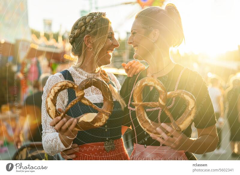 Two girlfriends together holding pretzel or brezen on a Bavarian fair or oktoberfest or duld in national costume or Dirndl in germany woman party beergarden