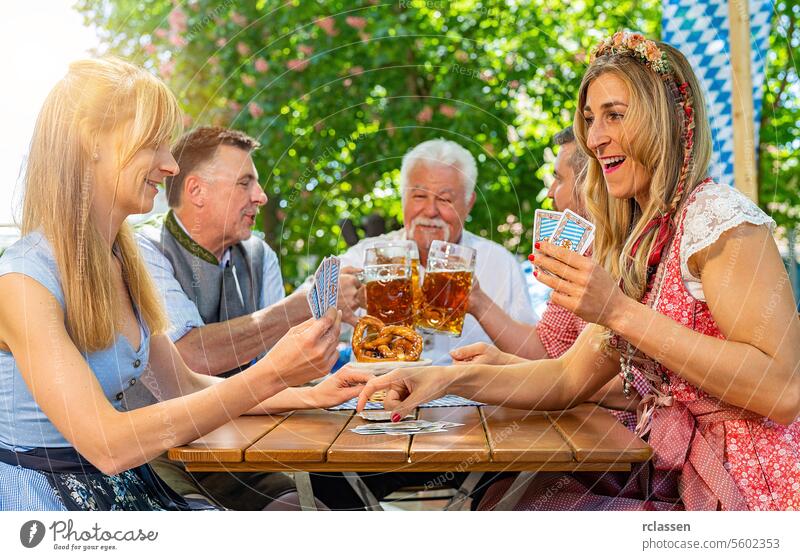 Bavarian people in traditional costume playing cards in beer garden or oktoberfest gambling card game blockhead cheer on pretzels friends woman grandfather