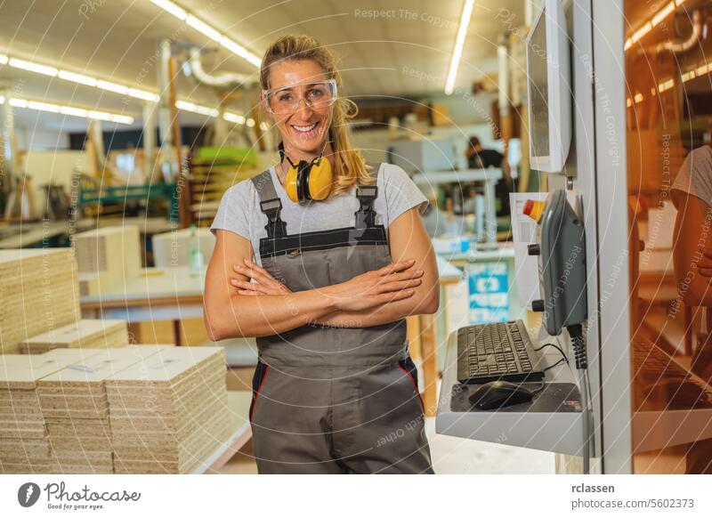 Confident woman with crossed arms and hearing protection in a carpentry workshop professional craftsman furniture industry worker wooden timber earmuffs