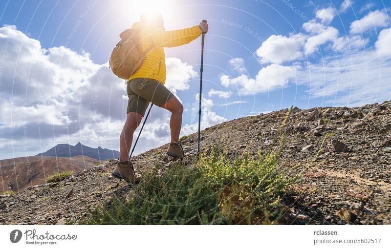 Hiker with backpack and trekking pole ascending a mountain trail under a cloudy sky fuerteventura hiker ascent hiking adventure outdoor wilderness