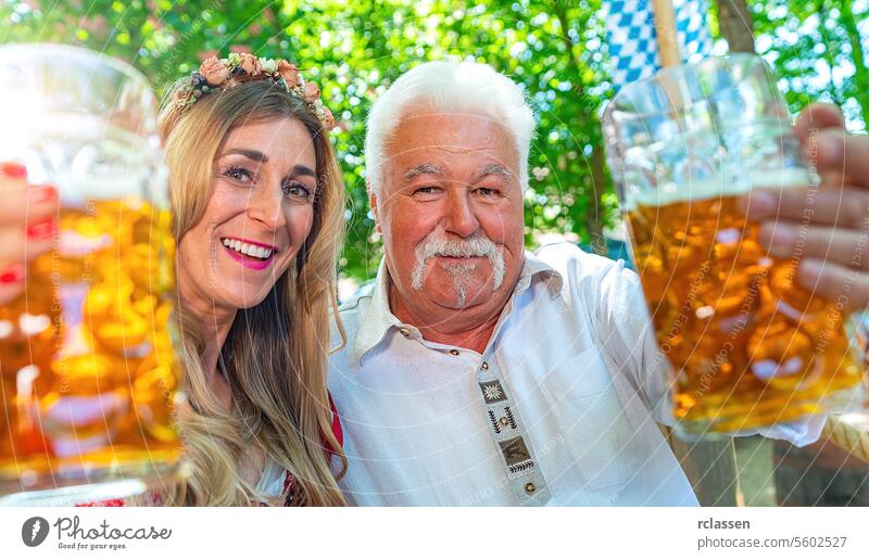 Old man and youn girl looking at camera say cheers or clinking glasses with mug of beer in Bavarian beer garden or oktoberfest pensioner old grandfather woman