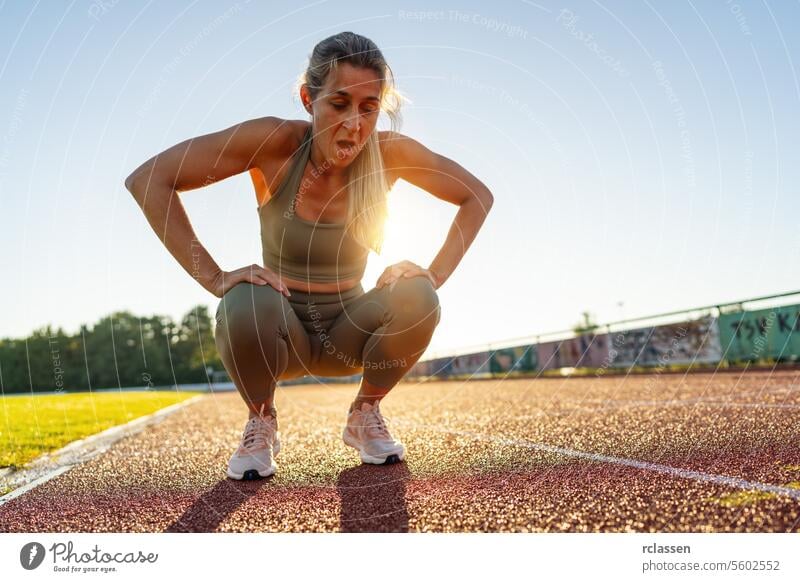 Tired female athlete resting on track field after workout exhaustion sportswear fitness training active lifestyle breath recovery outdoor exercise