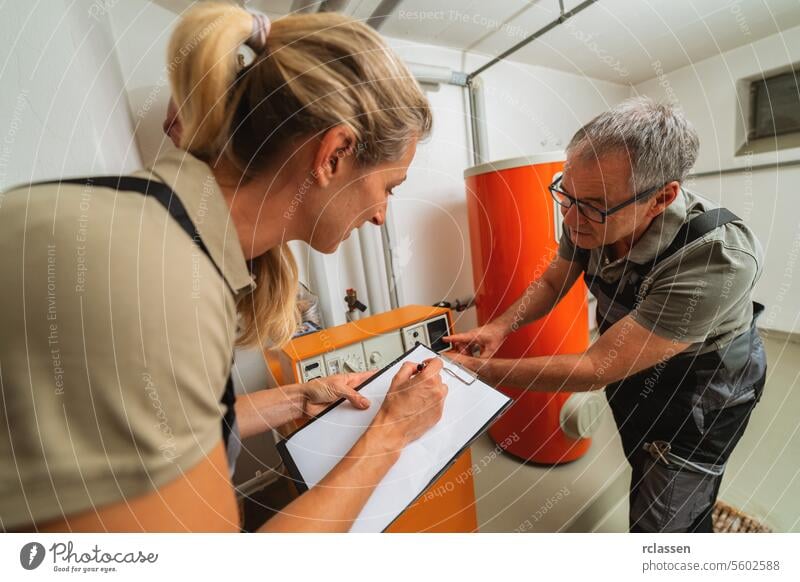 Heating engineers discussing and checking a old gas heating system, holding a Clipboard with checklist at a boiler room in a house. Gas heater replacement obligation concept image