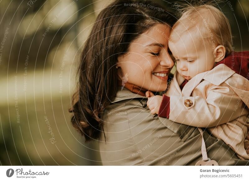 Young woman holding cute baby girl in the autumn park small caucasian mother outside daughter child little love happiness together family play mom smile season