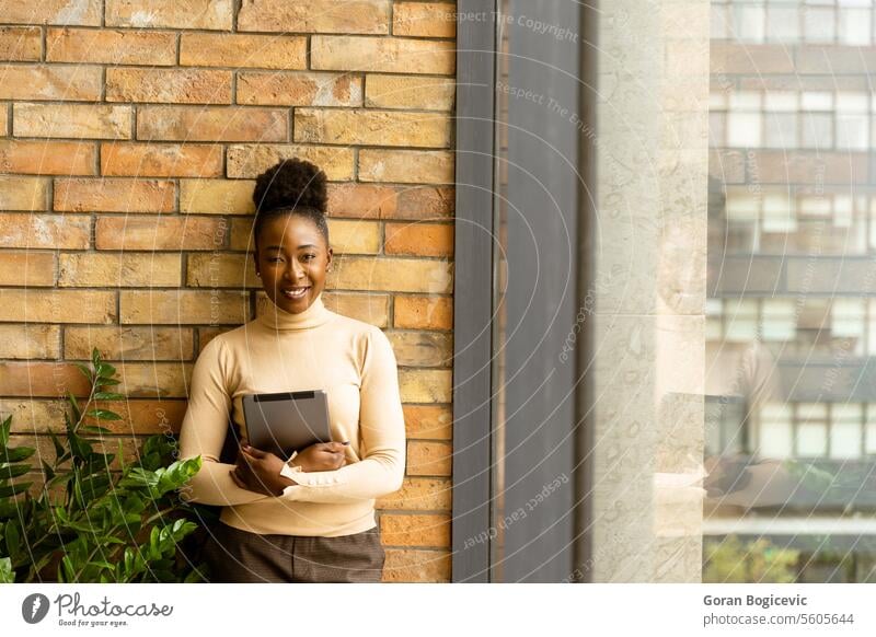 One young African American business woman with digital tablet standing by the brick wall in the industrial style office adult african american black