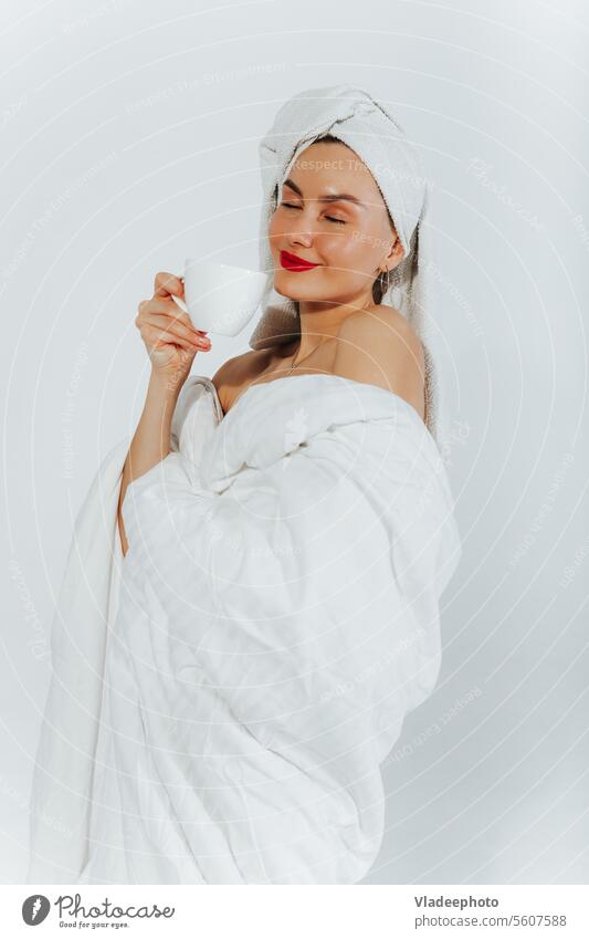 Woman wrapped in a blanket and a towel on her head enjoys a cup of coffee in the morning woman white tea young lifestyle female weekend beautiful caucasian