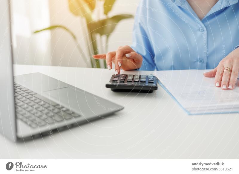 Unrecognisable businesswoman calculates on calculator expenses, fees, analyses financial reports, does accounting, paperwork job, laptop on desk at office. Investment, savings, currency concept