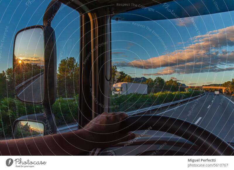 View from the driver's seat of a truck of a highway at dawn and the sun reflected in the rearview mirror. hand inside steering wheel rear-view mirror