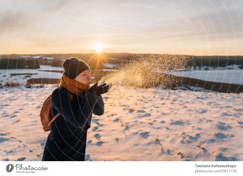 A woman on a snow-covered winter field blows snow off her palms female people person European White adult hold mid adult one Single person orange cold Enjoy