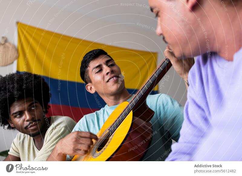 Male friends with guitar and flag at home colombian lifestyle together music play sit from below looking smile leisure free time talent relax carefree content