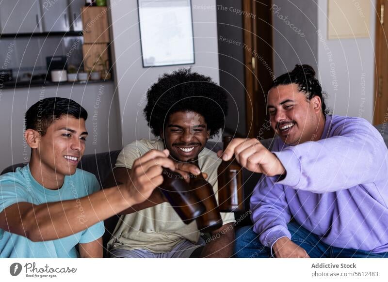 Happy diverse friends enjoying drinks at home toasting beer bottle cheerful living room alcohol weekend holiday friendship smile together lifestyle multiracial