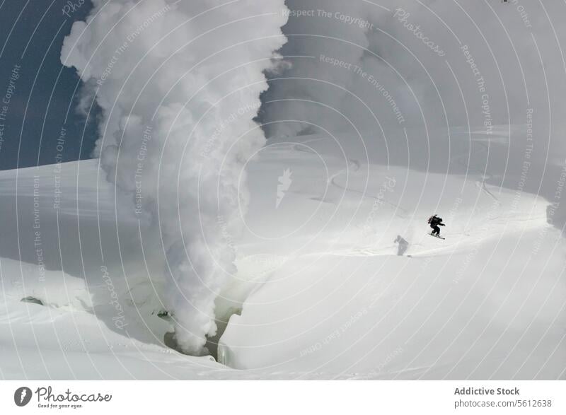 Full body of active unrecognizable person snowboarding on snow covered mountain slope with volcanic eruption in background during sunny day in winter vacation