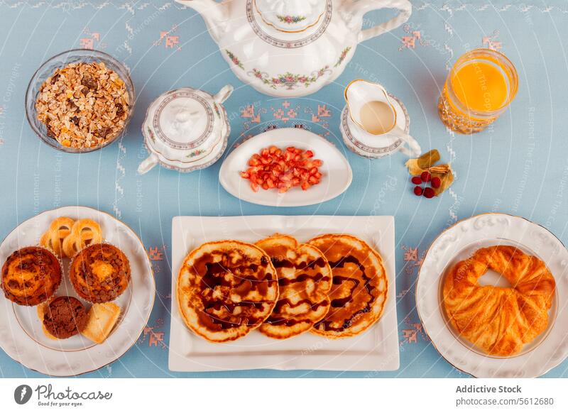 Healthy Breakfast Spread on a Blue Table breakfast blue table healthy orange juice tea granola cereal milk teapot cup fruit nuts buns pastries plate bowl