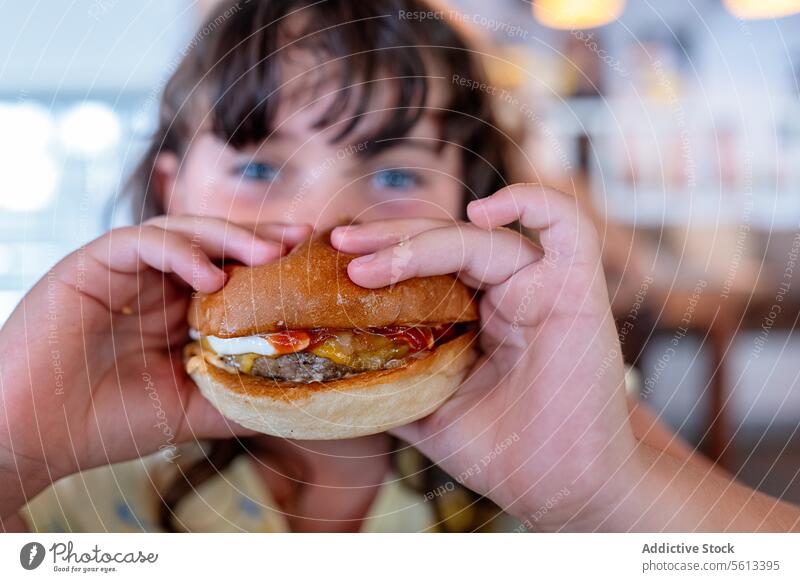 Closeup hands of hungry anonymous girl holding and eating delicious hamburger and looking at camera while spending leisure time in cafe innocent meal person