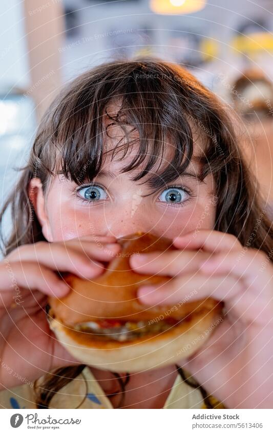 Closeup hands of hungry anonymous girl holding and eating delicious hamburger and looking at camera while spending leisure time in cafe innocent meal person