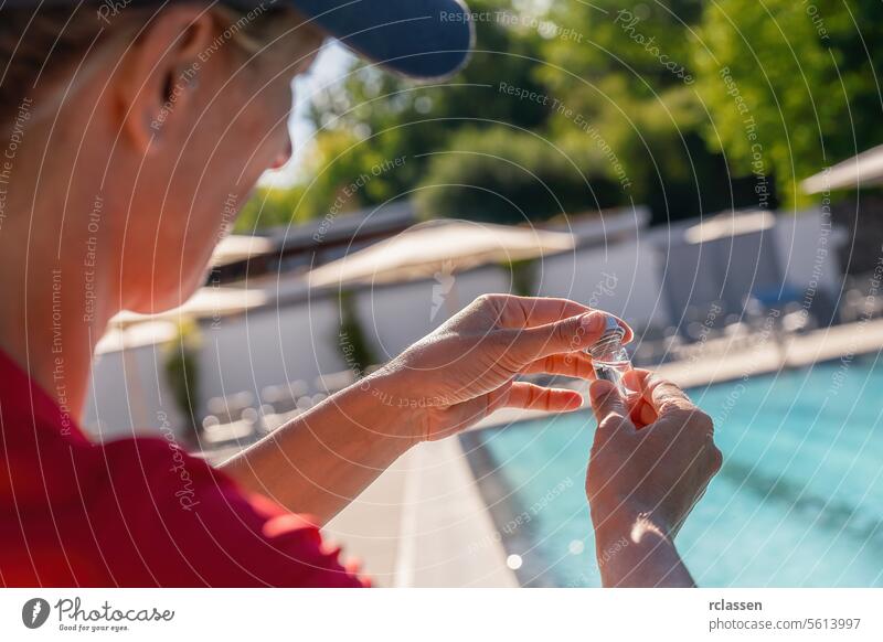 Close-up of woman's hands closing a small vial for PH value test with swimming pool in background bottling pool water testing water vial chlorine measure sample