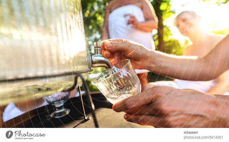 Close-up of hand pouring water from a dispenser with people in the background finnish sauna exhaustion lime lemon close-up beverage dispenser hydration