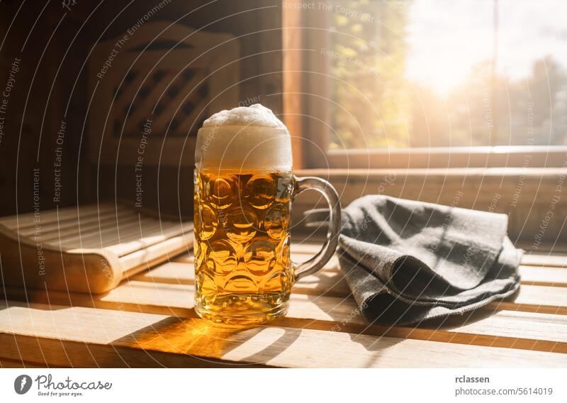 Beer mug with frothy beer rest on a ledge in a sauna, catching sunlight. Nearby finnish Sauna hats on a wooden bench. spa and wellness concept image interior