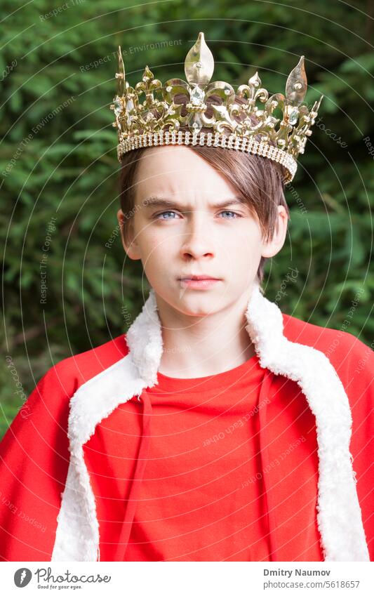 Portrait of teenager boy wearing crown and red cape pretending to be a king Facial Expression adolescent arrogant authority carnival child childhood confident