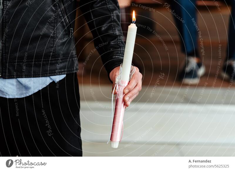 Detail of a man's hand holding a lit candle in church. Concept of the sacrament of Christian baptism. Burning pink baptismal candle. Baptism baptismal font