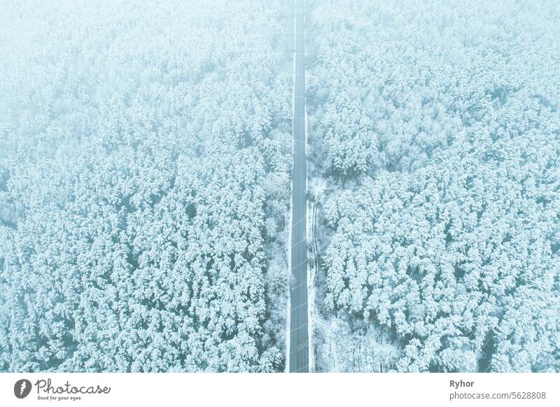 Aerial view of highway road through snow forest landscape in winter. Top view of highway motorway freeway from high attitude. Trip and travel concept scene