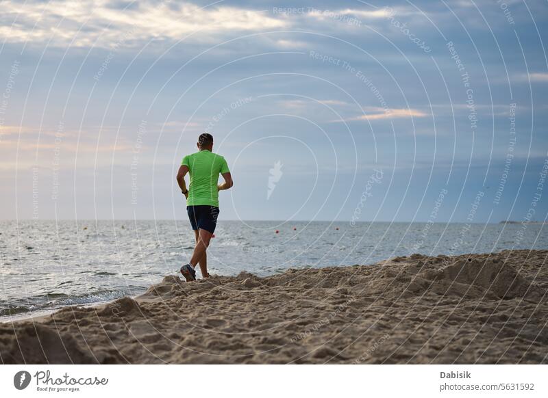 Back view of man jogging along sea beach at morning sport run runner coast lifestyle exercise cardio workout active athlete athletic baltic body fitness freedom