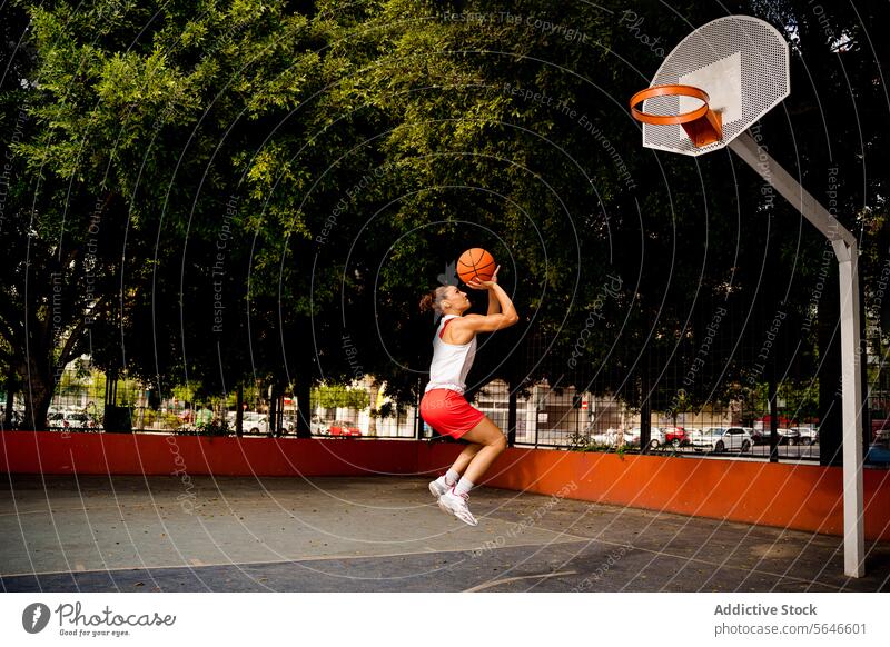 Full length side view of determined young female in sportswear jumping and throwing ball to make basket while playing on court Sportswoman Basketball Throw Jump